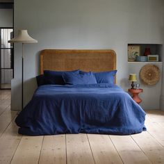 a bed with blue linens and pillows in a gray room next to a lamp