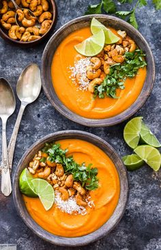 two bowls filled with carrot soup topped with cashews and cilantro leaves