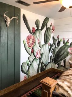 a large cactus mural painted on the side of a wall next to a wooden bench