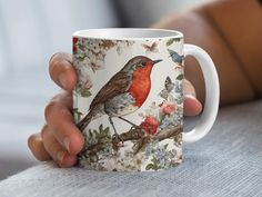 a person holding a coffee mug with a bird on it's side and flowers in the background