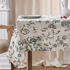 a table with a white vase on top of it next to a flowered table cloth