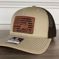 Deer Hunting American Flag Patriotic Leather Patch Hat Khaki/Brown. Specifications: 🧢 Richardson original 112 trucker; adjustable for the perfect fit 🎩 60/40 cotton/polyester blend for comfort 📏 One size fits most 🏷️ Expertly laser engraved leatherette patch design 📦 Ships in 2 to 3 business days from our Orlando Studio Care Instructions: 🚫 Do not wash; spot clean only Please Note: 🌈 Colors may vary from photos based on your viewing screen. Khaki Cap For Fall, Brown Flat Brim Country Baseball Cap, Brown Flat Brim Country Style Baseball Cap, Khaki Hats For Outdoor Fall Use, Brown Outdoor Baseball Cap, Khaki Outdoor Hat For Fall, Brown Country Style Baseball Cap With Curved Brim, Country Style Brown Baseball Cap With Flat Brim, Country Style Brown Flat Brim Baseball Cap