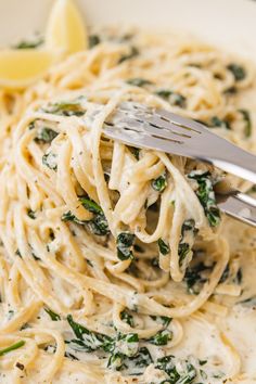 a fork full of pasta with spinach and lemon wedges on the side in a white bowl