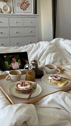 two plates with pancakes on them sitting on top of a bed next to a laptop