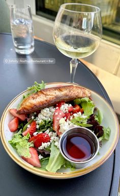 a plate with salad and fish next to a glass of wine