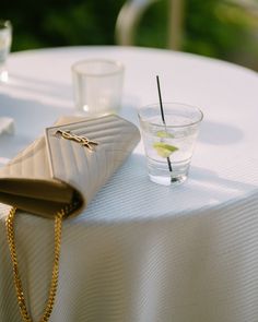 a white table topped with a gold purse next to a shot glass filled with water