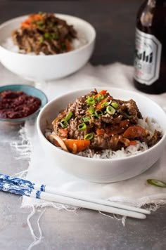 two bowls filled with rice, meat and veggies next to a bottle of beer