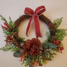 a wreath with pine cones and red berries is hung on the wall by a ribbon