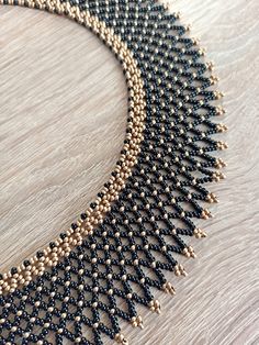 a black and gold beaded necklace on a wooden surface