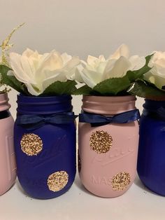 three mason jars with flowers in them are painted pink, blue and gold to match each other