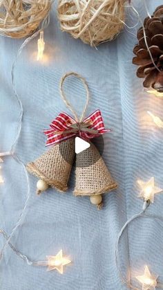 two christmas bells are hanging from twine with lights on the ground next to pine cones