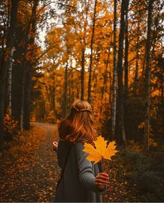 a woman walking down a path holding a leaf in her hand and looking up at the sky