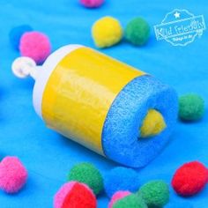 colorful pom - poms scattered around a tube of glue on a blue surface