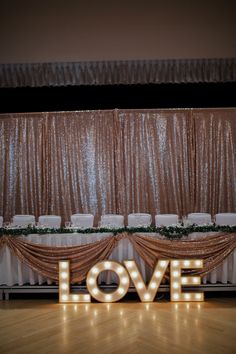 the word love is lit up in front of a stage with chairs and drapes