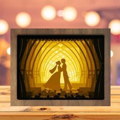 a wooden frame with a silhouette of a man and woman in front of a yellow light