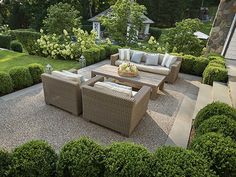 an outdoor living area with couches and tables surrounded by shrubbery, shrubs and trees