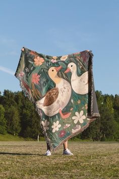 there is a woman holding a blanket with ducks on it in the grass and trees behind her