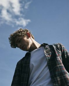 a young man standing in front of a blue sky with white clouds and his head tilted to the side