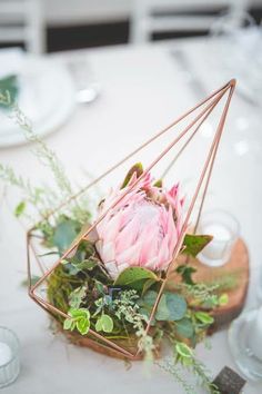 an arrangement of flowers and greenery in a geometric vase on a white table cloth