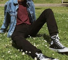 a man sitting in the grass wearing black and white converse shoes with his legs crossed