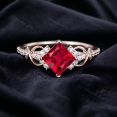 a ring with a red stone surrounded by white diamonds on a black cloth background, close up