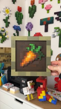 a person holding up a small pixel art piece in front of a wall full of legos