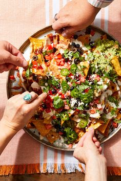 two people reaching for nachos on a plate with salsa and guacamole