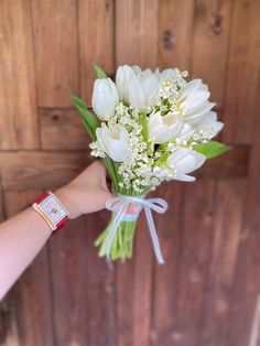 a bouquet of white tulips tied to a wooden wall with a person's hand holding it