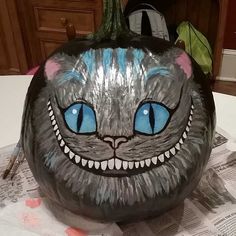 a painted pumpkin with a cat's face and blue eyes is on the table