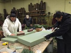 three people working in a pottery shop with lots of pots and plants on the table