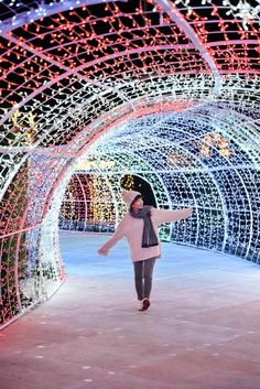 a woman is walking through a tunnel covered in christmas lights and snowflakes