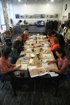 a group of people sitting around a table working on some art work in an art studio