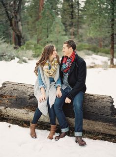 a man and woman are sitting on a log in the snow, looking into each other's eyes