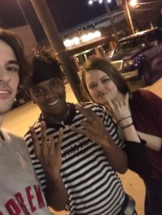 three people standing next to each other in front of a parking lot at night time