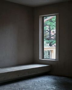 an empty room with a window and stone bench in the foreground, looking out onto trees