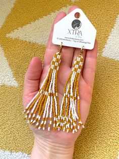 a pair of gold and white beaded tassels on a person's hand