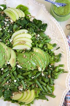 a white plate topped with green vegetables and sliced avocados