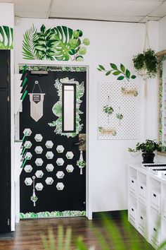 a black door decorated with green leaves and hanging plants on the wall next to it