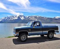 a truck parked on the side of a road next to a body of water with mountains in the background