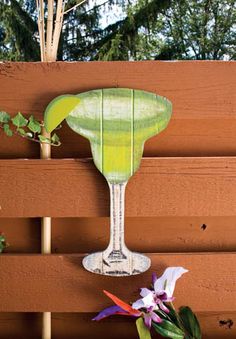 a wooden fence with a green glass vase and flowers on it's side next to a planter