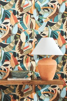 an orange vase sitting on top of a wooden shelf next to a wallpaper covered in colorful birds