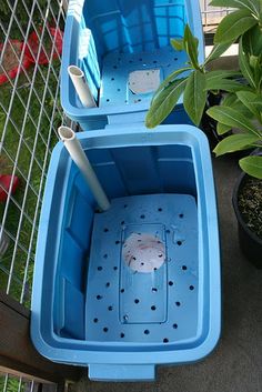 two blue plastic containers with holes in them sitting next to a potted plant and fence