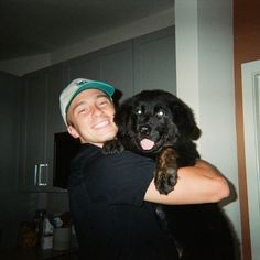 a man is holding a black dog in his arms and smiling at the camera while wearing a hat