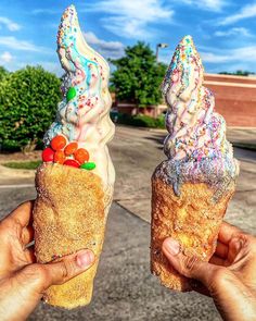 two people holding ice cream cones with sprinkles and candy toppings on them