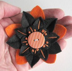 a hand holding an orange and black flower brooch with pins on it's center