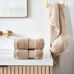 two towels are stacked on top of a white counter in front of a gold faucet