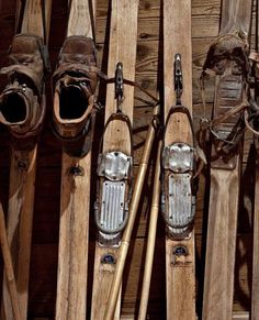 several pairs of skis are lined up against a wooden wall with leather shoes on them