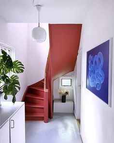 a red staircase leading up to a white room with paintings on the wall and potted plant