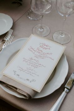 a table set with wine glasses, silverware and menu card on it's place setting