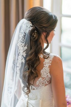 a bride in her wedding dress looking out the window with her veil draped over her head